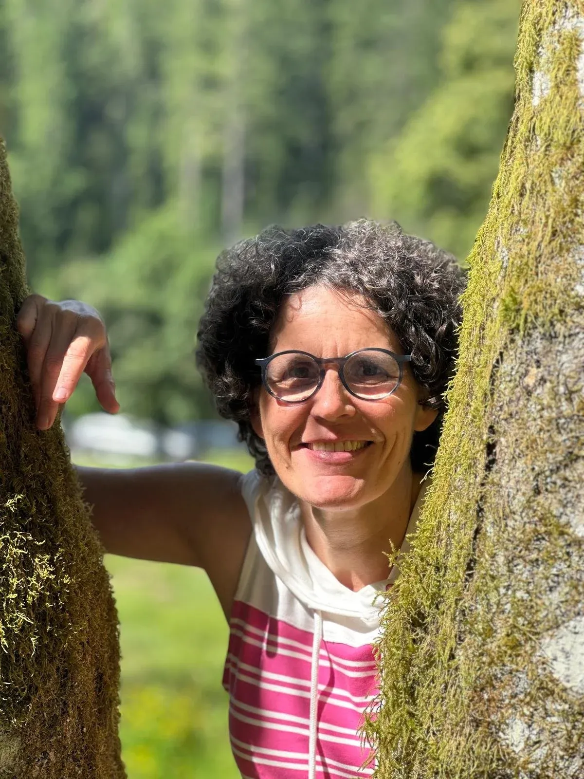Stefanie Mischka im Freien, zwischen zwei bemoosten Baumstämmen hervorschauend